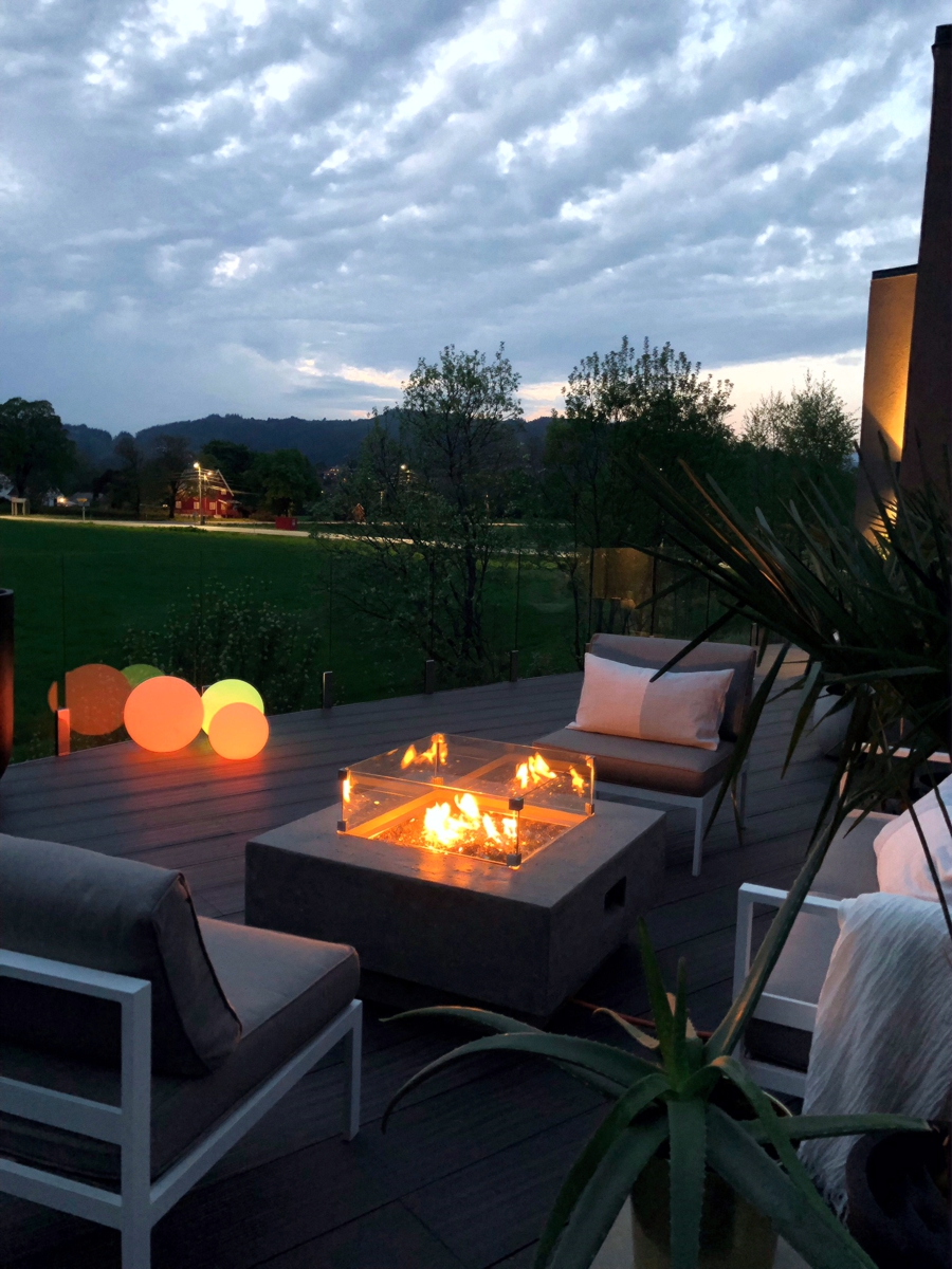 Feuerstelle mit Windschutz aus Glas abends auf der Terrasse