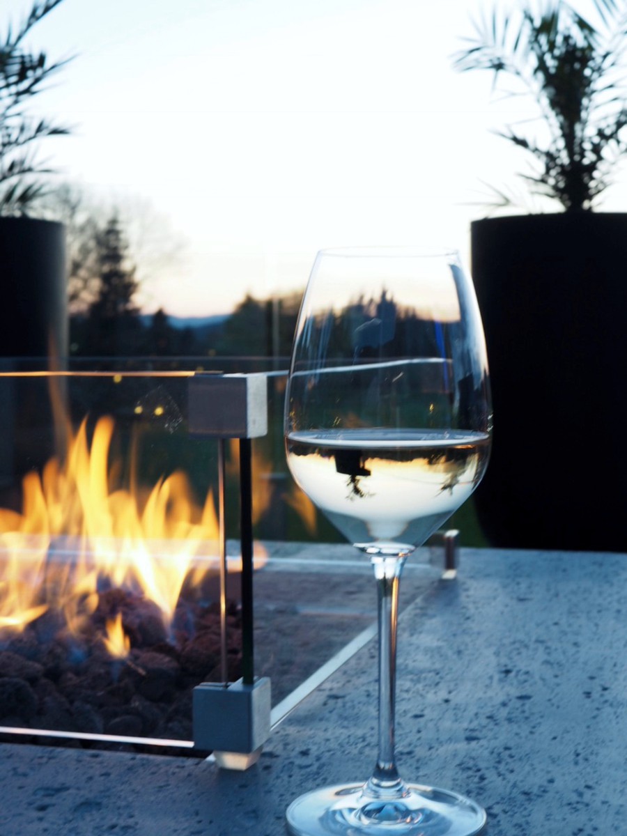 Windschutz aus Glas am brennenden Feuer mit einem Glas Wein