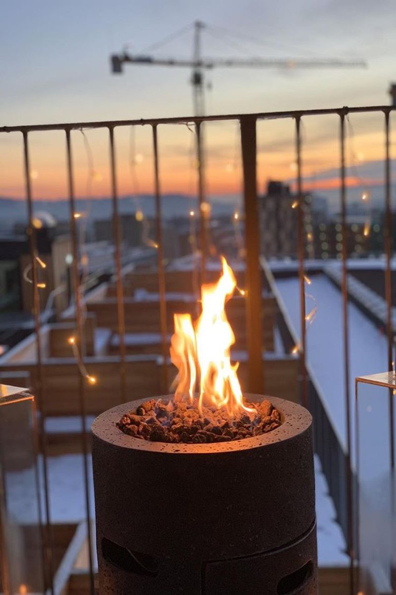 Feuerstelle LAVA TUBE mit brennendem Feuer auf einem Balkon bei Sonnenuntergang
