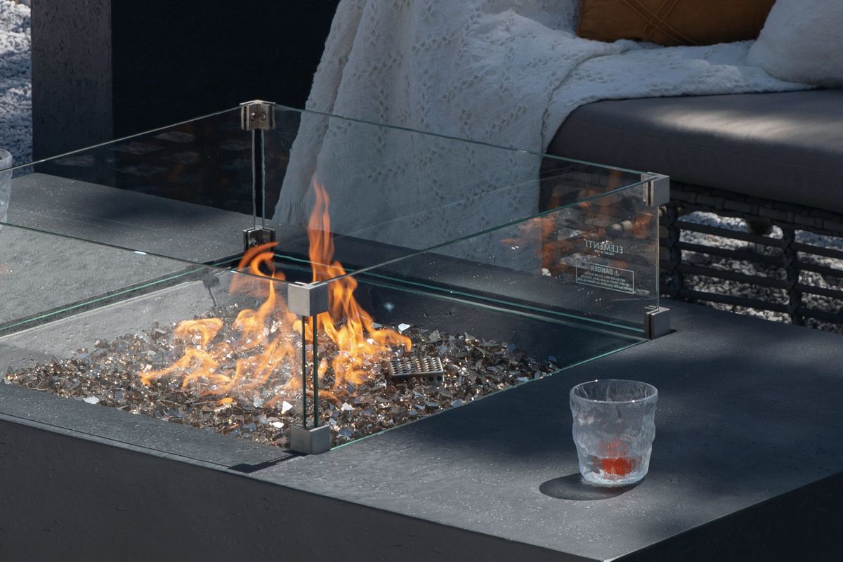 Brennende Feuerstelle des Tisches CANNES mit Windschutz aus Glas