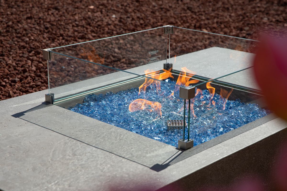 Brennende Feuerstelle des Tisches MONTE CARLO mit Windschutz aus Glas