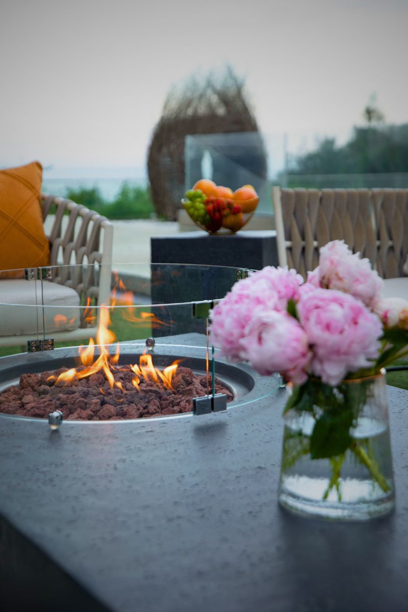 Brennende Feuerstelle des Tisches METROPOLIS Dark Grey mit Windschutz aus Glas und Blumen