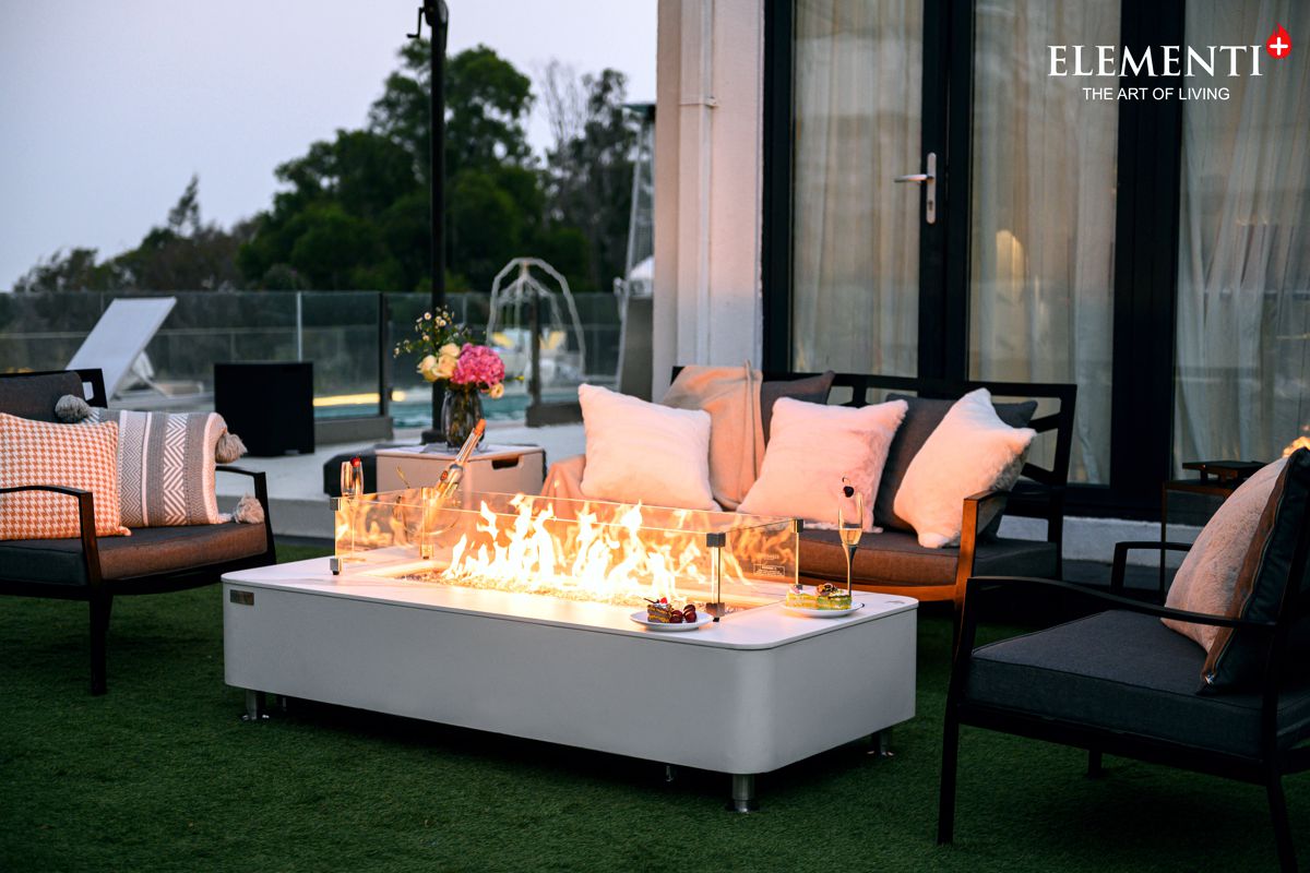 Tisch ATHENS mit brennendem Feuer auf der Terrasse vor einem Sofa