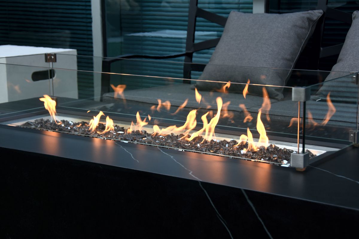 Brennende Feuerstelle des Tisches VARNA mit Windschutz aus Glas